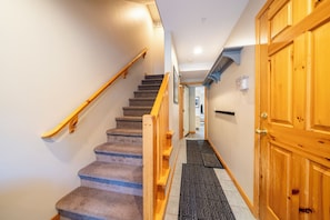 A carpeted staircase with wooden handrails leading to a door. - Alpine Retreat in Village Core, Sleeps 8 (Sun Peaks)