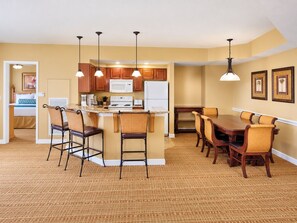 A compact kitchen with a central island, bar stools, and a dining table with chairs. - Bonnet Creek Resort - Spacious 1 BR Presidential near Lake Buena Vista (Lake Buena Vista)