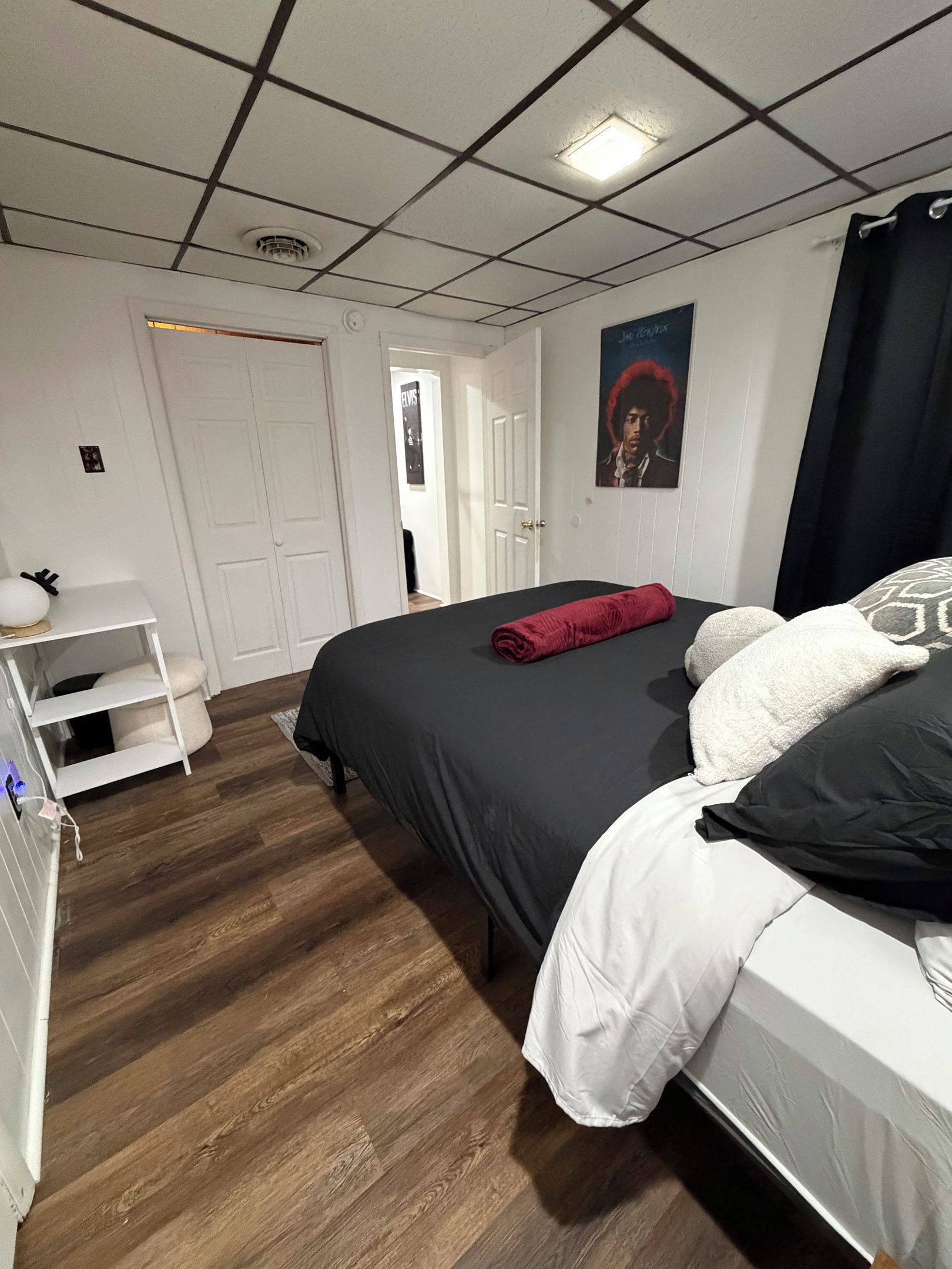 A bedroom with a bed, a white wardrobe, a shelf with a lamp, and a poster on the wall.