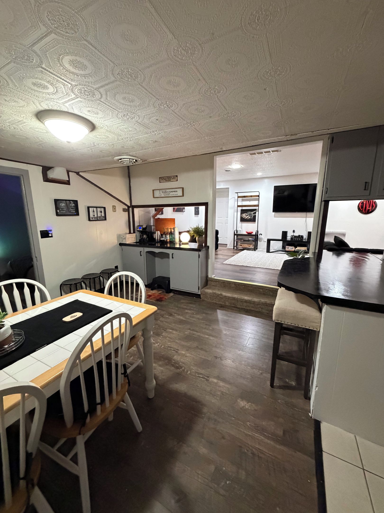 A dining area with a wooden table and chairs, a kitchen with a counter and appliances, and a living area with a TV and seating.