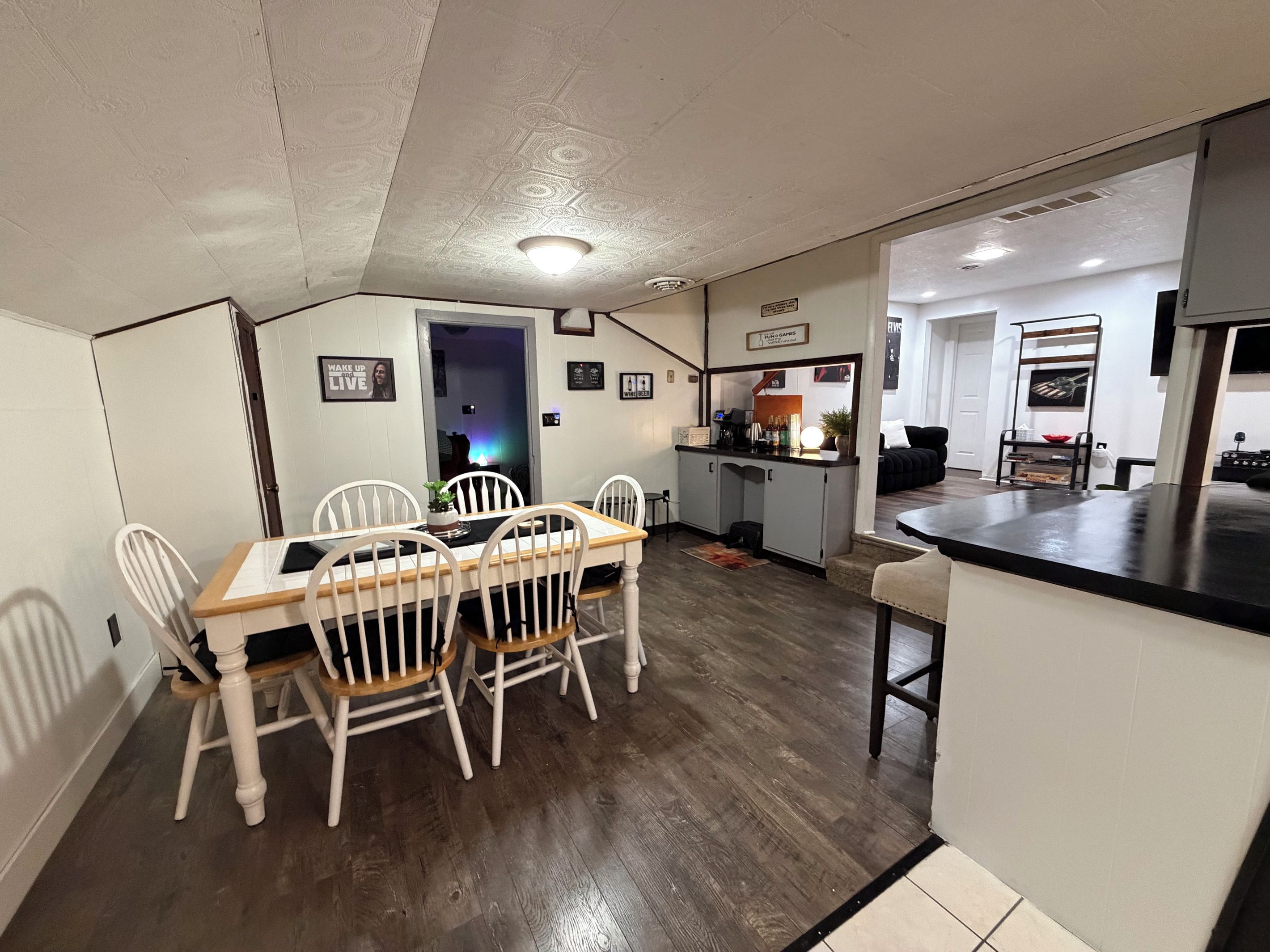 Un comedor con mesa de madera y sillas blancas, una cocina con barra y una sala de estar con sofá y mesa de centro.