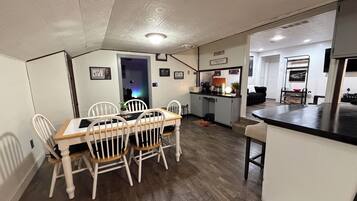 Un comedor con mesa de madera y sillas blancas, una cocina con barra y una sala de estar con sofá y mesa de centro.