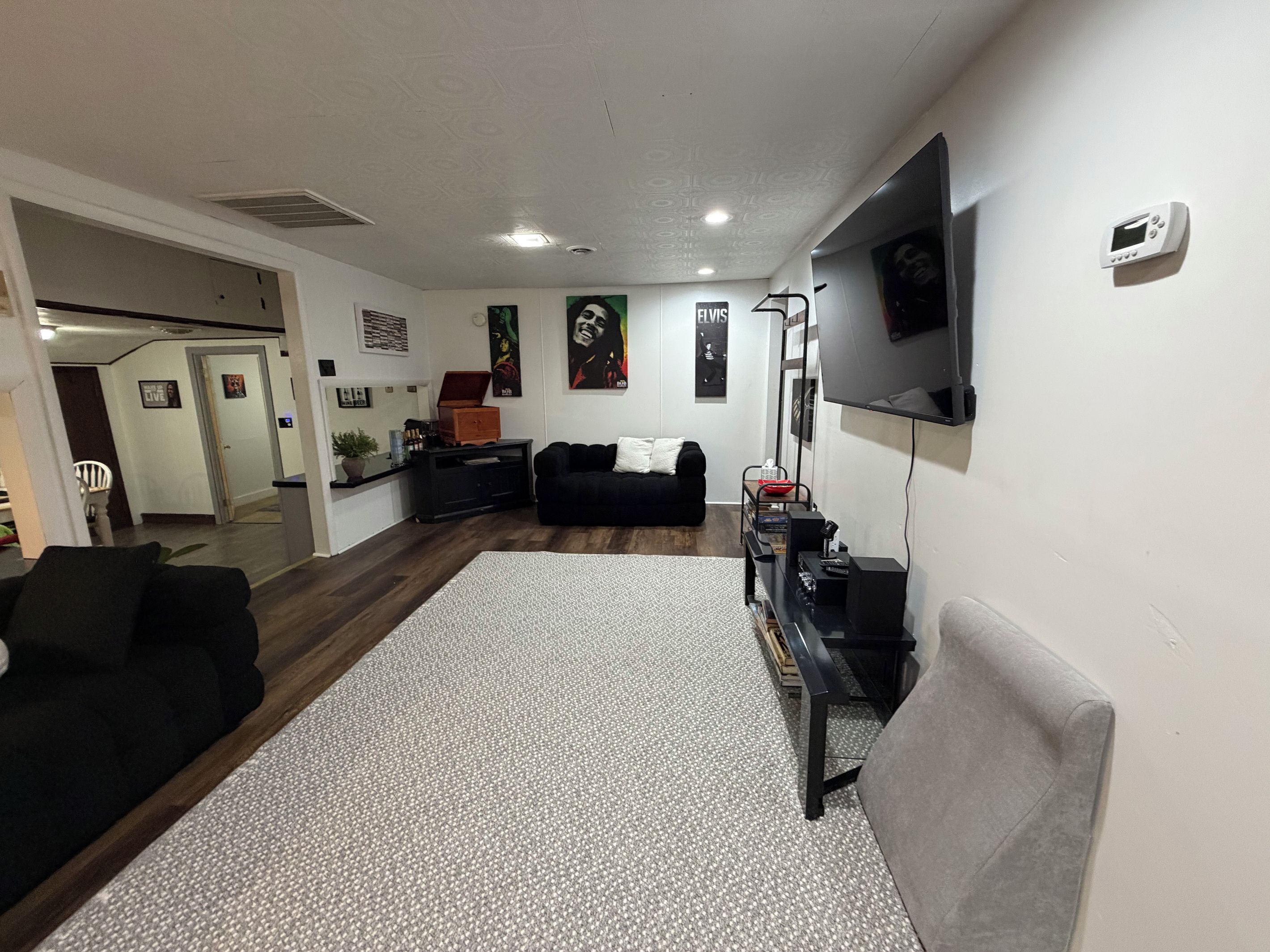 A living room with a black sofa, a grey armchair, a coffee table, and a flat-screen TV mounted on the wall.