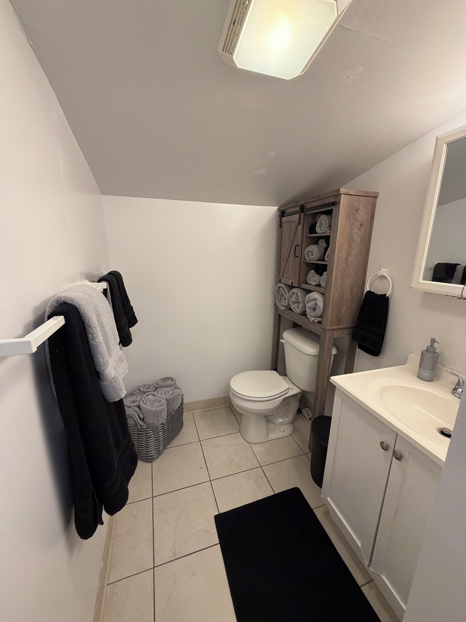 A compact bathroom with a toilet, a sink, a towel rack, and a wooden shelf with towels.