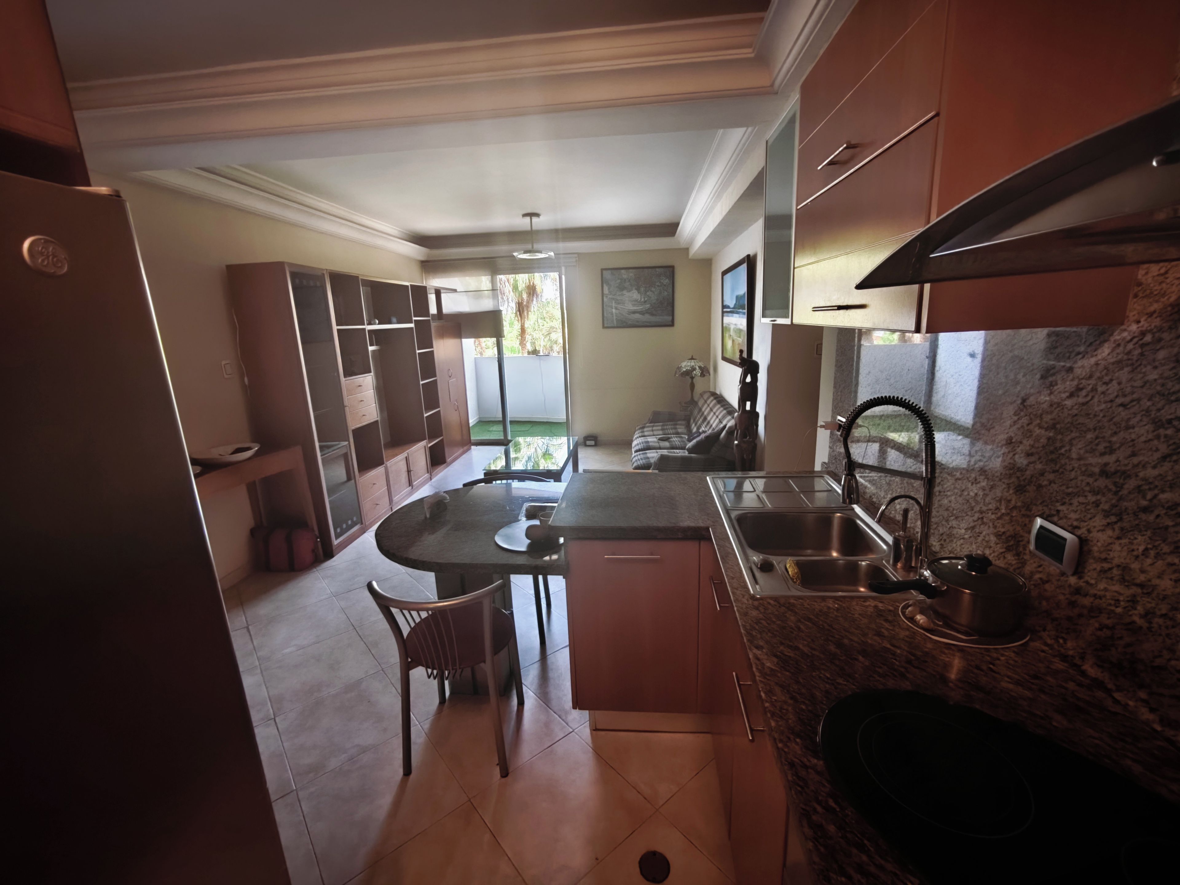 A kitchen with a granite countertop, stainless steel sink, and a built-in oven. There is a dining area with a table and chairs.