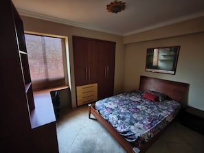 A bedroom with a bed, a wardrobe, a window with blinds, and a ceiling fan.