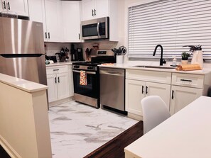 A modern kitchen with white cabinets, stainless steel appliances, and a marble floor. - Retreat Near Virginia-Highland! (Atlanta)