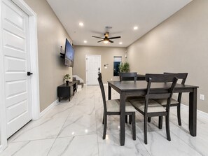 Un comedor con una mesa, sillas, un ventilador de techo y un televisor en la pared.