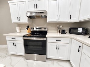 Una cocina con armarios blancos, horno de acero inoxidable y microondas.