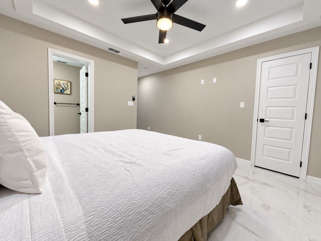 A bedroom with a bed, a ceiling fan, a door, and a light fixture.