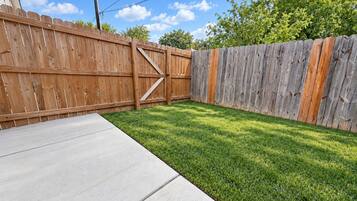 A backyard with a wooden fence, a concrete patio, and a well-maintained lawn.