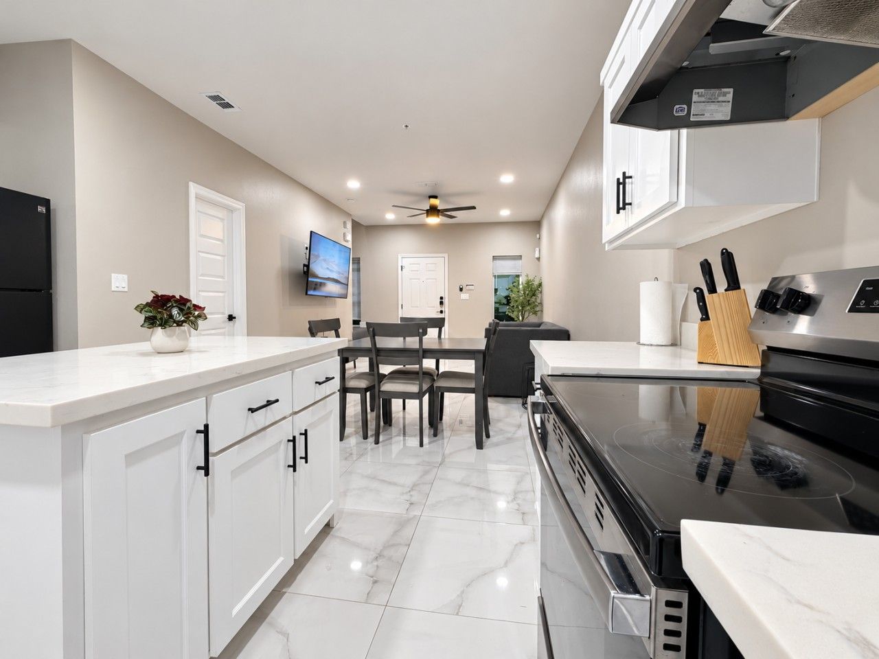 Une cuisine moderne avec des meubles blancs, une cuisinière noire et un coin repas comprenant une table et des chaises.