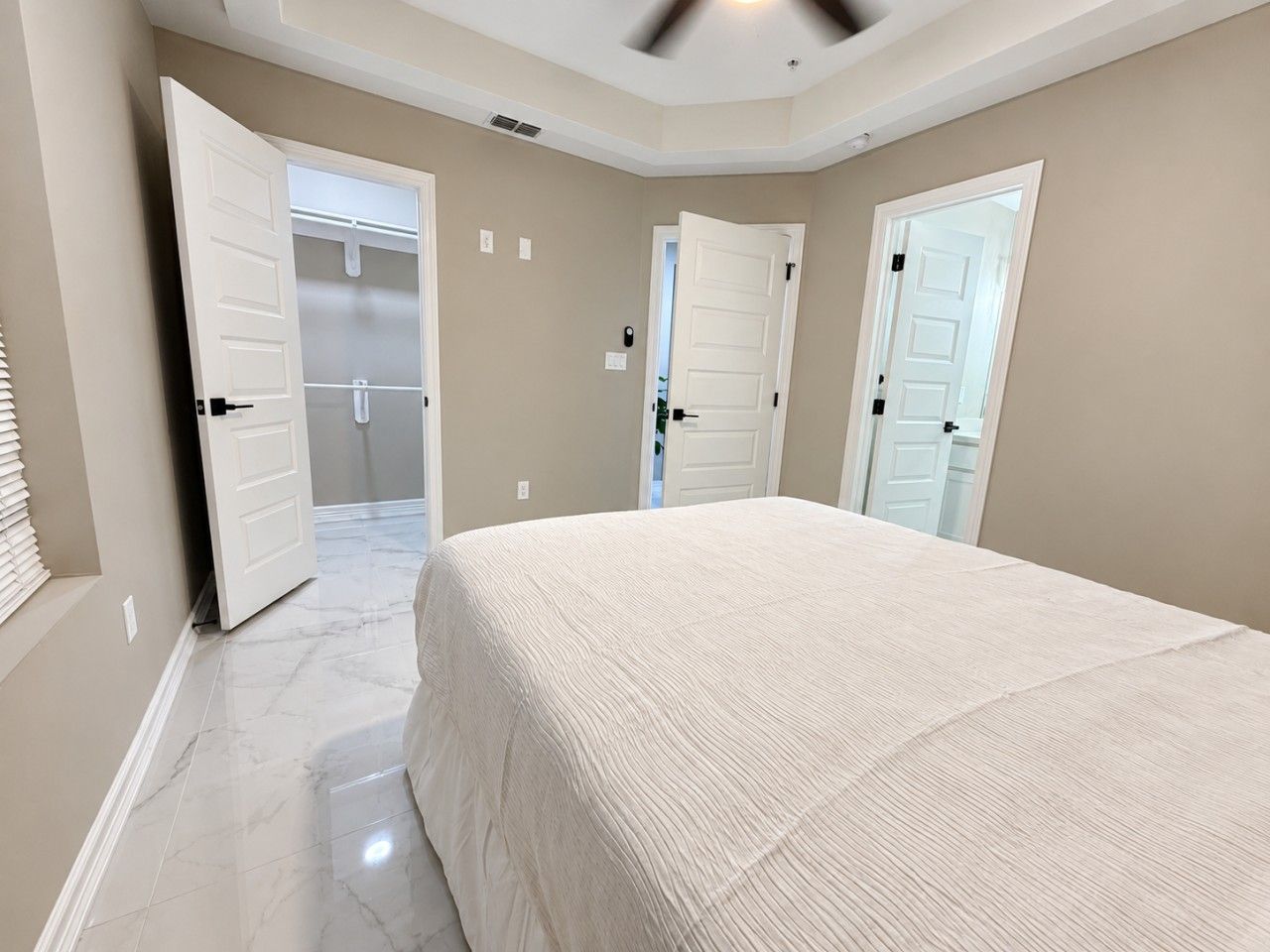 A bedroom with a large bed, two doors, and a ceiling fan.