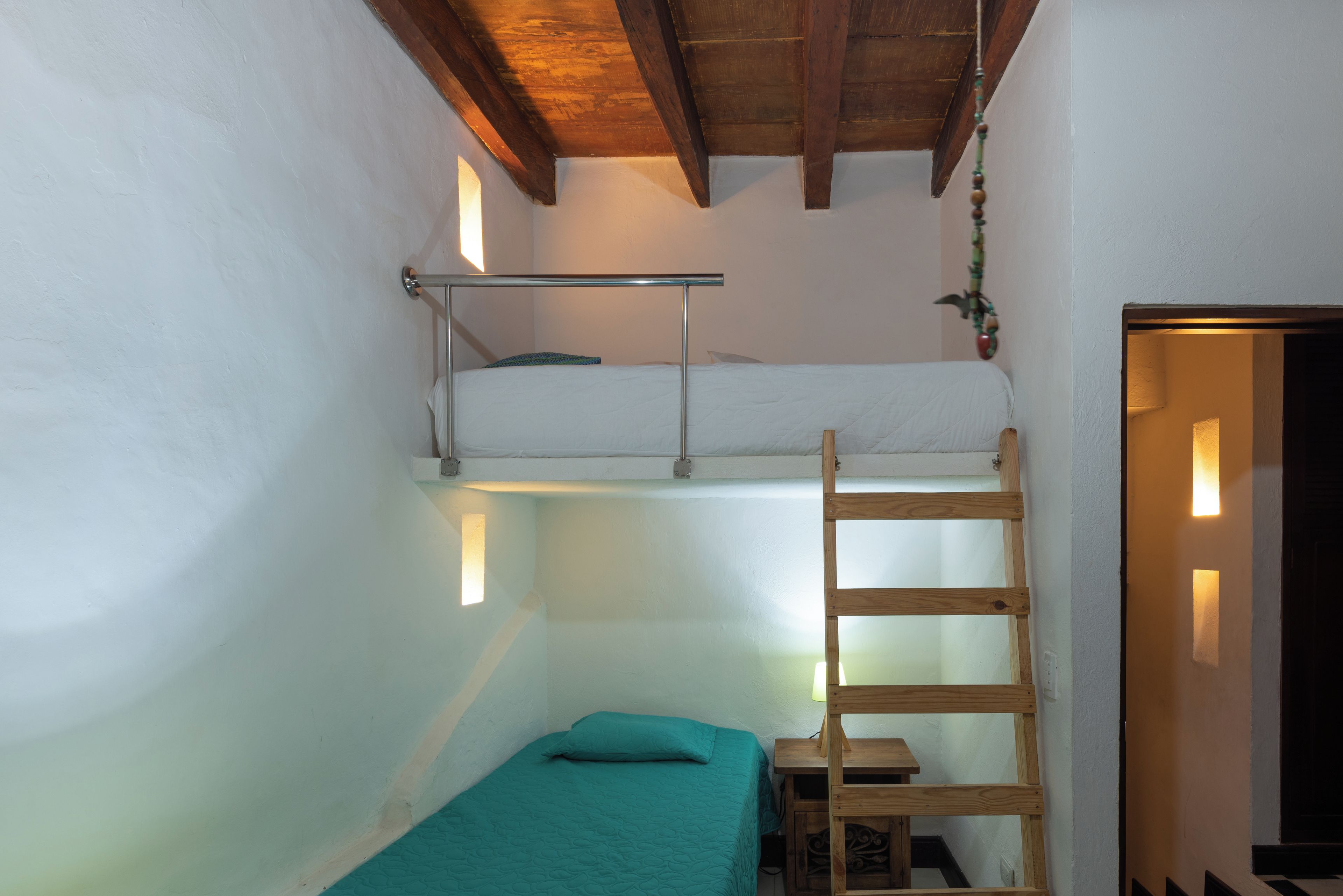 Habitación tipo dormitorio con literas, una escalera, un escritorio y una mesita.