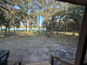 Une vue depuis un espace abrité, avec un banc en bois, une poubelle et un sentier menant à un lac entouré d’arbres.