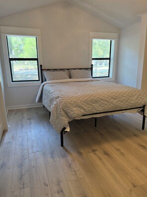 A bedroom with a bed, two windows, and wooden flooring. - Peaceful 3-bedroom house in Lake Tawakoni (Quinlan)