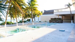 A pool area with clear water, surrounded by palm trees and a building with a flat roof. - Casa de Playa Xpu Ha Beach (Xpu-Ha)