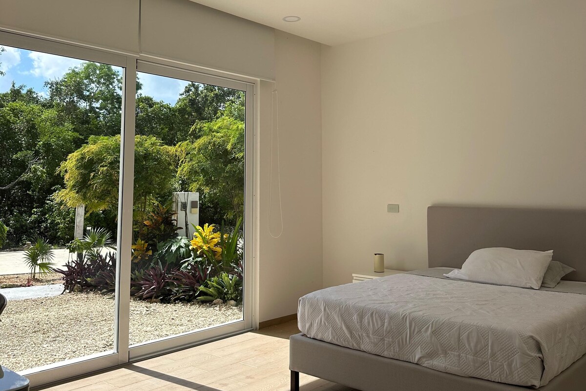 A bedroom with a bed, a ceiling fan, and a view of greenery outside.