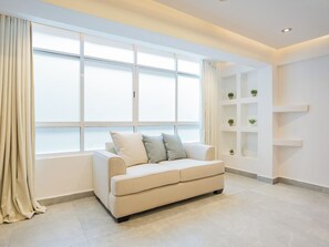 En moderne stue med sofa, stort vindue med persienner og indbyggede reoler med planter.