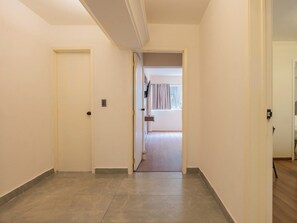 A hallway with a closed door on the left, a door leading to a room with a window and curtains on the right, and a wooden floor. - Stylish 2BR in Polanco with King Bed and Workspace (Mexico City)