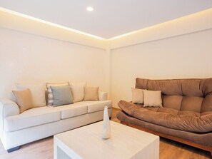 Ein modernes Wohnzimmer mit einem weißen Sofa und einem braunen Sofa, beide mit vielen Kissen. Eine weiße Vase steht auf einem weißen Couchtisch.