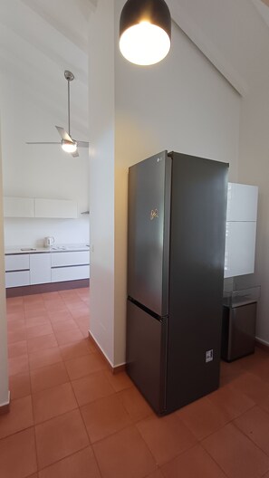 Eine Küche mit einem schwarzen Kühlschrank, weißen Schränken und einem Deckenventilator.