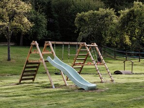 A playground with a slide and swings in a grassy area. - Harmony Homes | Caorches Le Voisnard - Heated indoor pool, 1h50 from Paris (Caorches-Saint-Nicolas)