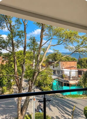 A view from a window overlooking a street with trees, a parked motorcycle, and buildings in the background. - New Listing (Medellín)