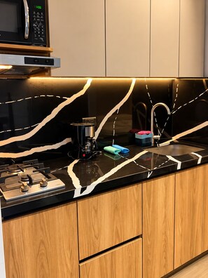 Una cocina moderna con encimera negra, armarios de madera, cafetera y microondas.