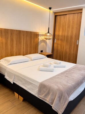 A modern bedroom with a large bed, wooden headboard, bedside tables, and a hanging light fixture. - New Listing (Medellín)