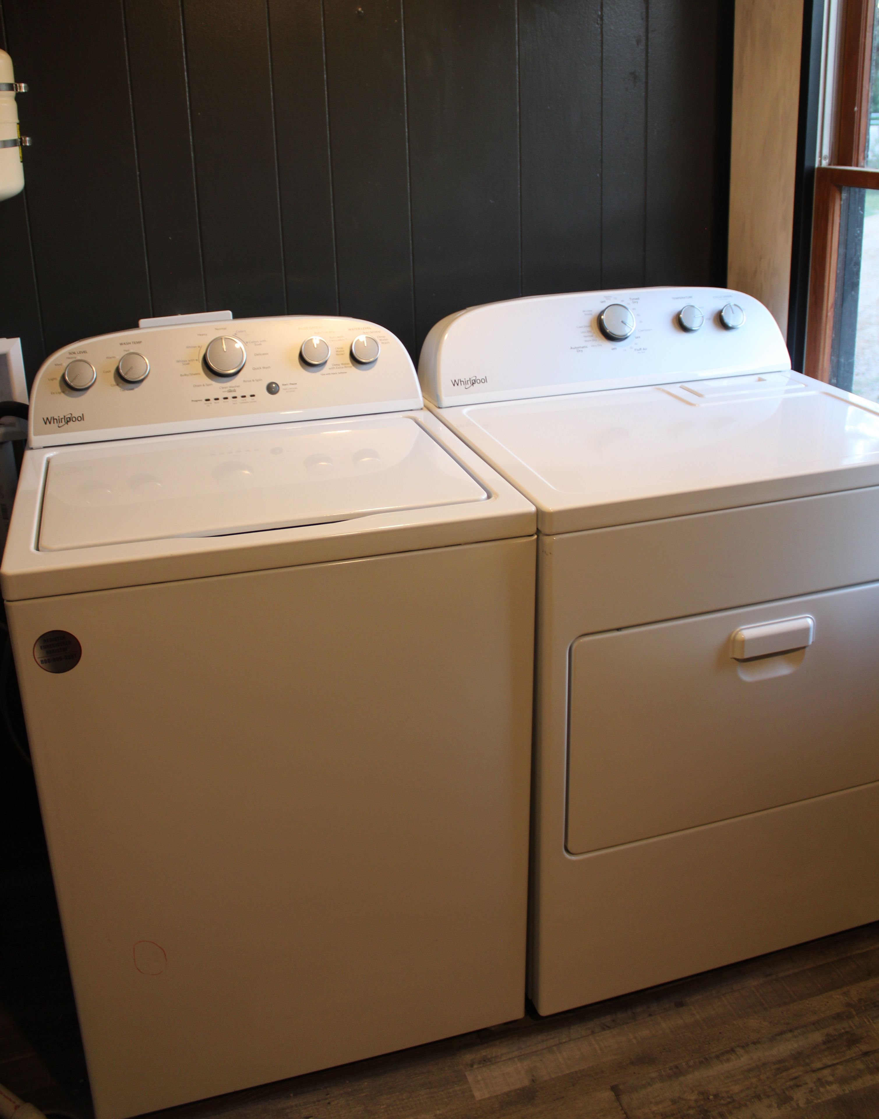 A white Whirlpool washer and dryer in a room with wooden flooring and a black wall.