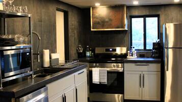 A modern kitchen with stainless steel appliances, a wooden ceiling, and a view through a window.