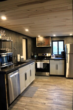 A modern kitchen with stainless steel appliances, a wooden ceiling, and a view through a window.