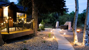 Un espacio exterior moderno con terraza de madera, sendero de piedra e iluminación ambiental.