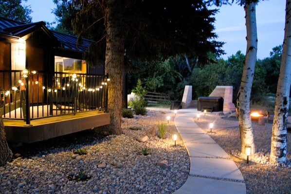 A modern outdoor area with a wooden deck, stone pathway, and ambient lighting.