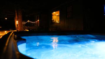 A nighttime view of a swimming pool with a wooden deck and a building with a lit interior.