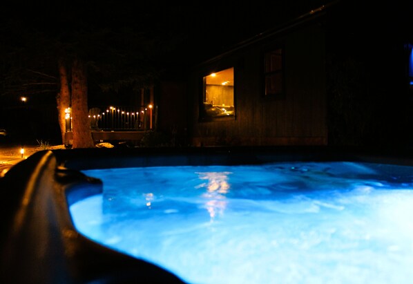 A nighttime view of a swimming pool with a wooden deck and a building with a lit interior.