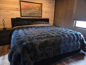 A bedroom with a bed, a nightstand, a wall-mounted painting, and a window.
