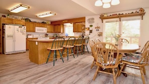 A kitchen with wooden cabinets, a central island with bar stools, a refrigerator, and a dining table with chairs.