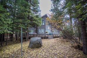 A cabin with a deck, surrounded by trees and a large rock in the foreground.