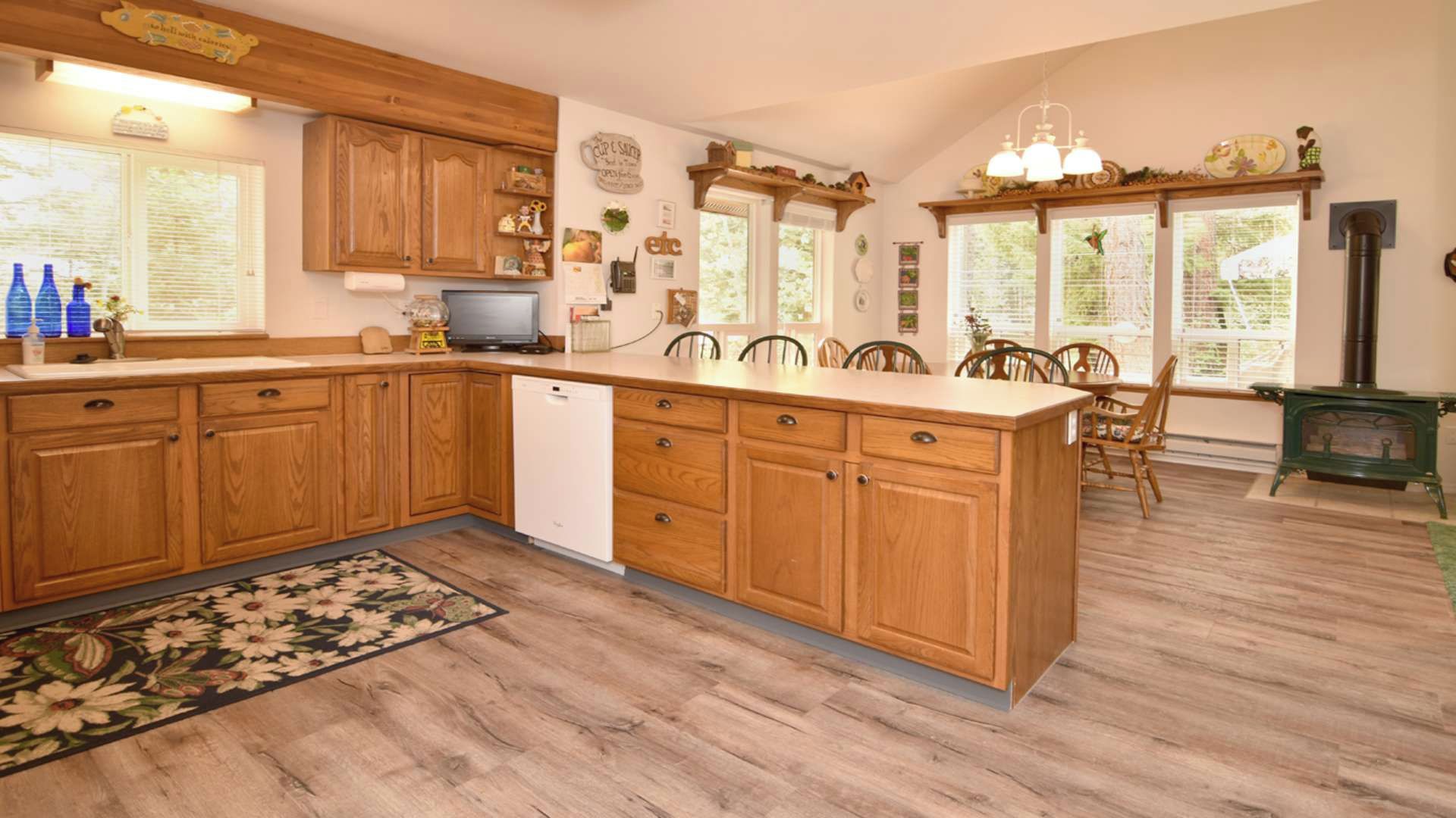 Una cocina con armarios de madera, una isla central, lavavajillas empotrado y un comedor con sillas y una mesa.