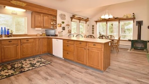 A kitchen with wooden cabinets, a central island, a built-in dishwasher, and a dining area with chairs and a table.