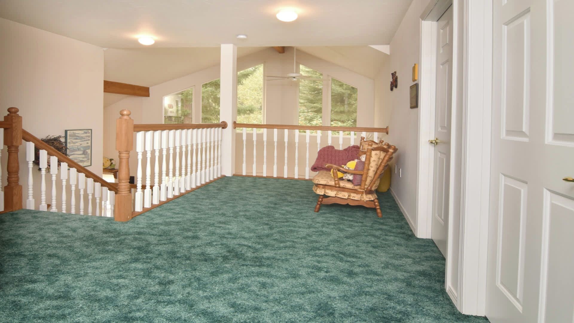 A room with a green carpet, a wooden chair, a white railing, and a door.
