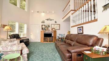 A living room with a brown leather sofa, a floral-patterned couch, a wooden entertainment unit, and a staircase with white balusters.