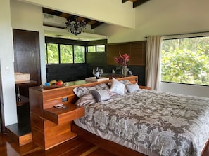 A bedroom with a large bed, wooden bedside tables, a built-in bench, and a view of greenery outside. - Beauty of Costa Rica by Pura Villas (Bahía Ballena)