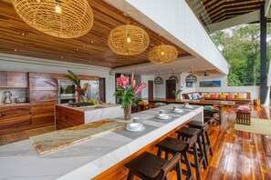 Een moderne keuken met een groot schiereiland, houten kastjes en hangende rieten kroonluchters.