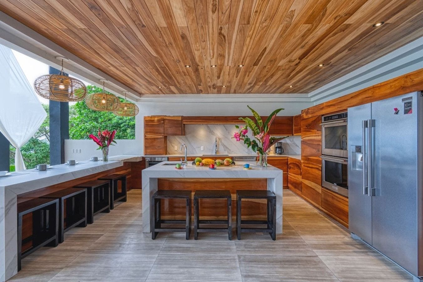 A modern kitchen with a wooden ceiling, a central island with stools, and stainless steel appliances.