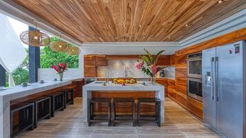 A modern kitchen with a wooden ceiling, a central island with stools, and stainless steel appliances.
