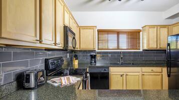 A kitchen with granite countertops, wooden cabinets, a black refrigerator, a microwave, a toaster, and a dishwasher.