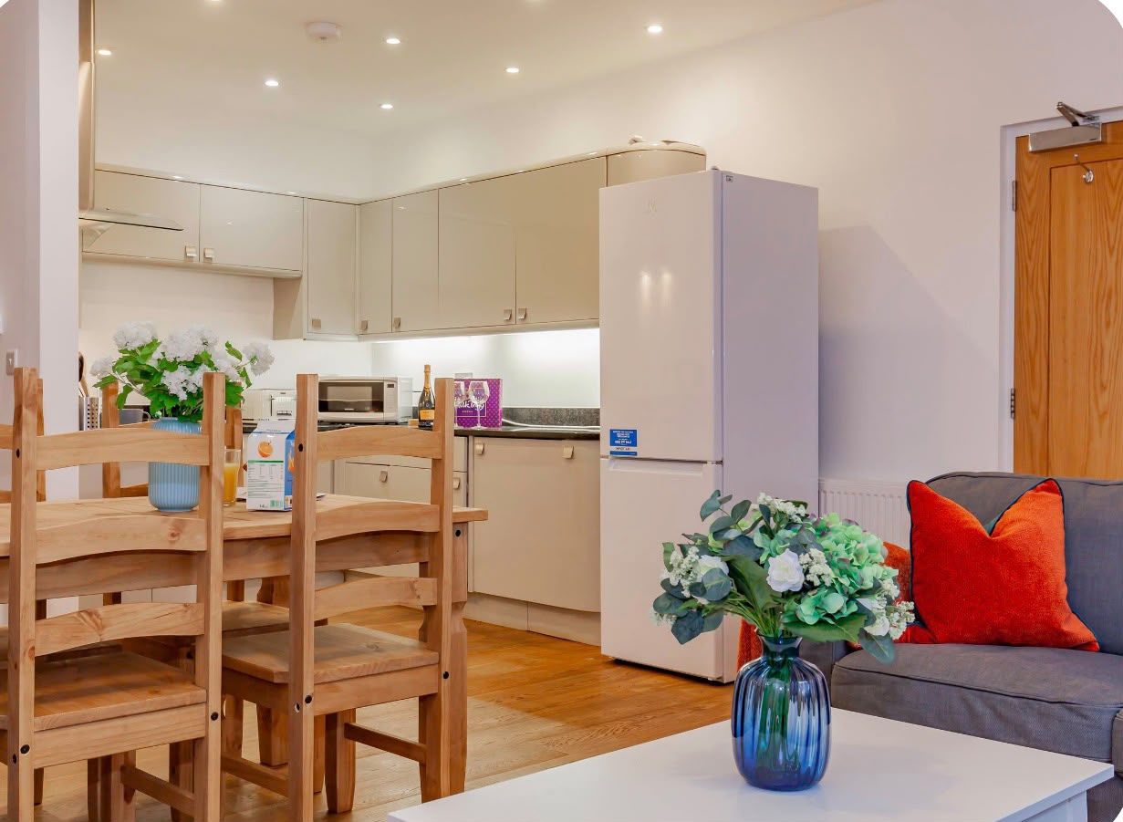 A modern kitchen with white cabinets, a refrigerator, and a dining area with wooden chairs and a table.